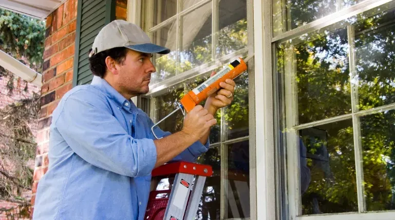 Man sealing gap in window